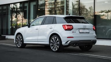 Rear three-quarter view of the white crossover showing the tail lights and roof spoiler. Car 87