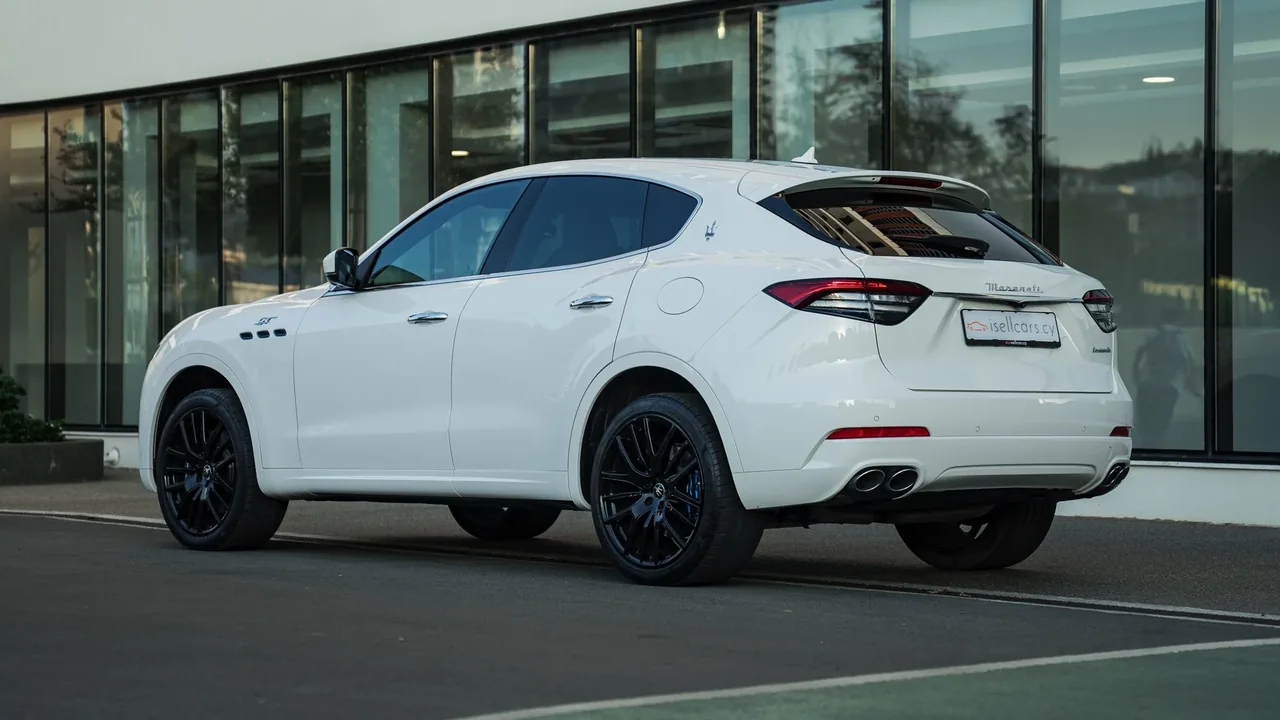 Rear three-quarter view of the white crossover by a glass facade. Car 93