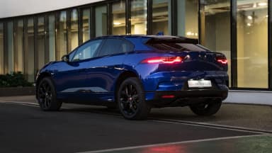 Rear three-quarter view of the blue crossover by a glass facade in evening light. Car 88