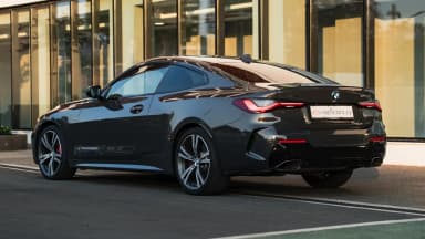 Rear three-quarter view of the black coupe by a glass facade. Car 90