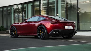 Rear three-quarter view of the coupe by a glass facade. Car 92